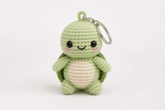 Handmade crochet turtle keyring with light green body, pink cheeks, and a keychain attached