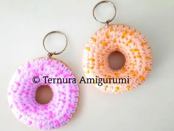 Two crocheted donut keychains with pink and purple frosting and embroidered sprinkles on a white surface.
